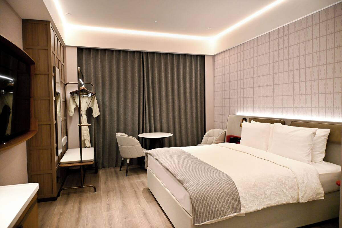 Une chambre d’hôtel avec un grand lit, une petite table ronde, une chaise, un téléviseur et une armoire.