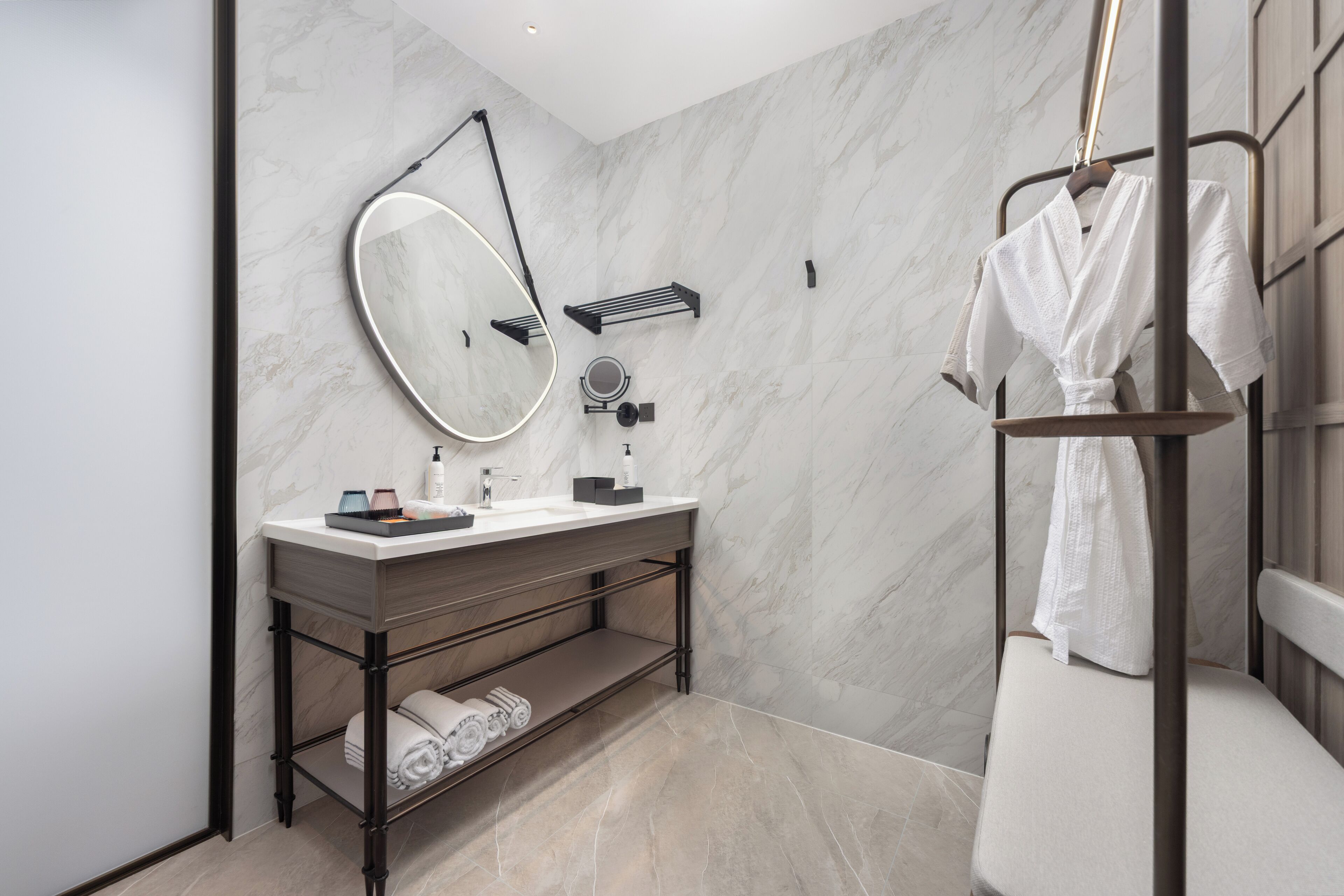 A modern bathroom with a marble wall, a large mirror, a vanity with a sink, and a towel rack.