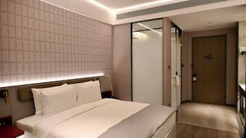 Una habitación de hotel moderna con una cama grande, mesitas de noche, un armario y un baño con puerta de cristal.