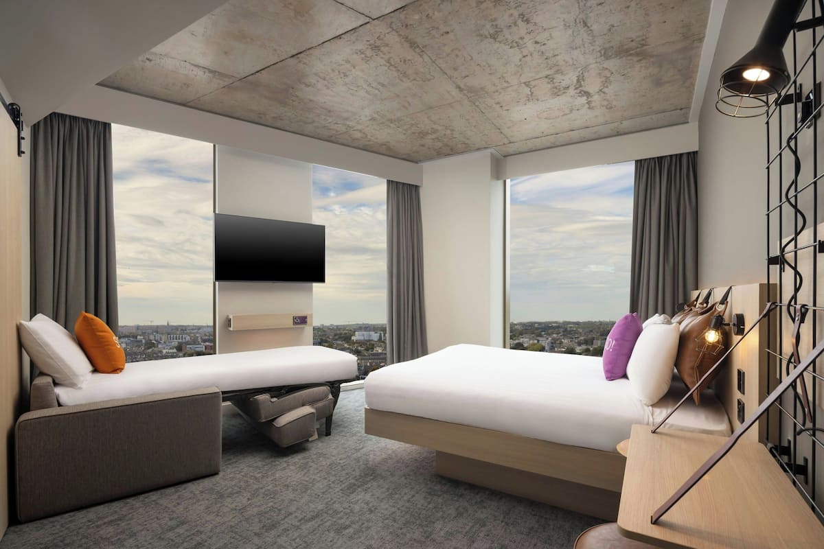 Ein modernes Hotelzimmer mit zwei Betten, einer Sitzecke, einem Fernseher und Blick auf die Stadt.