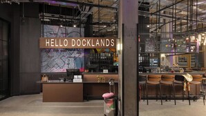 Un mostrador de recepción con un cartel que dice 'HELLO DOCKLANDS', un mapa y una zona de bar con taburetes.