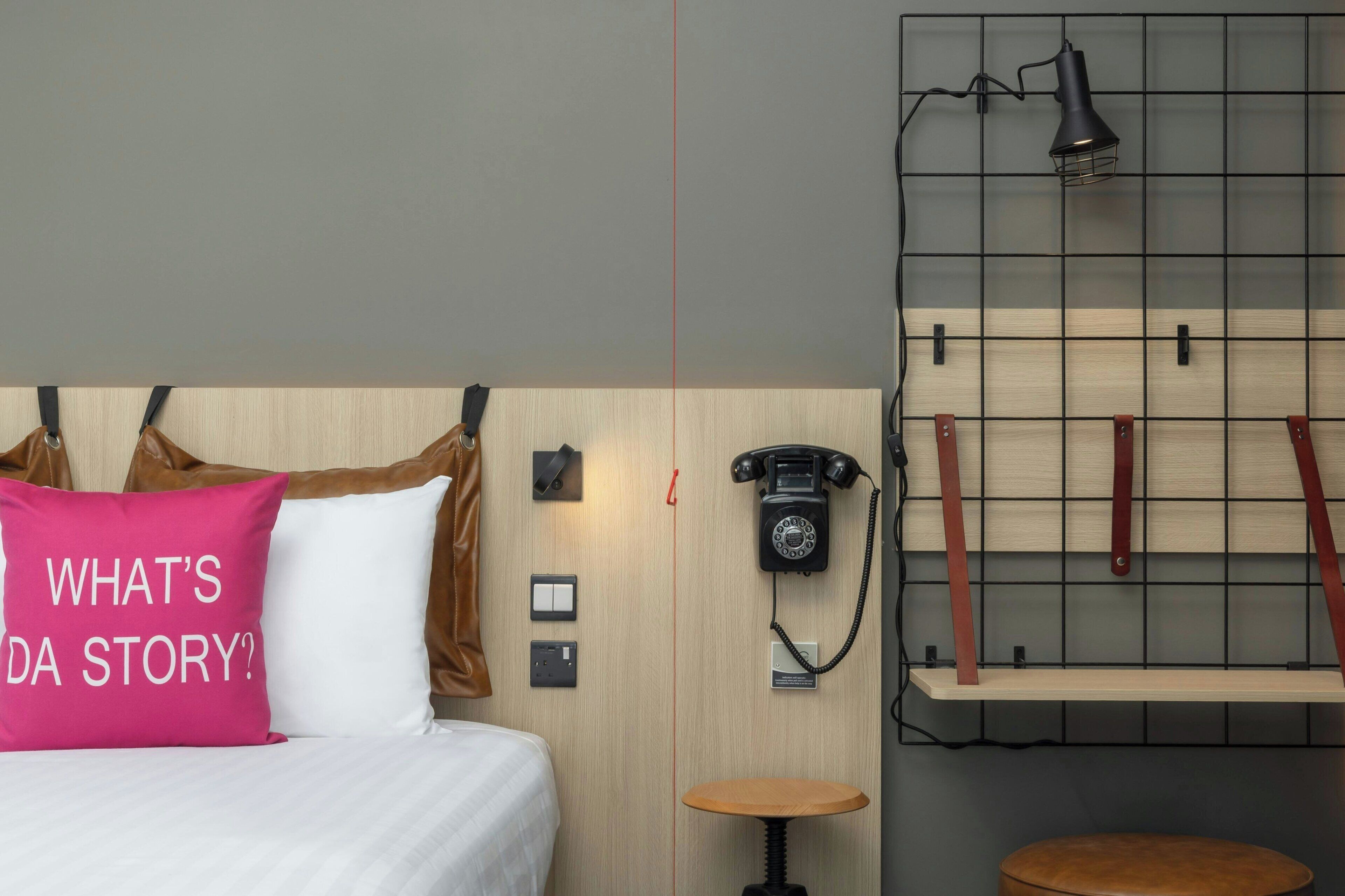 A hotel room with a bed, a red and white pillow, a telephone, a lamp, and a shelf.