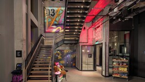 Un interior moderno con una escalera, un mural colorido, un letrero de neón y un estante con aperitivos.