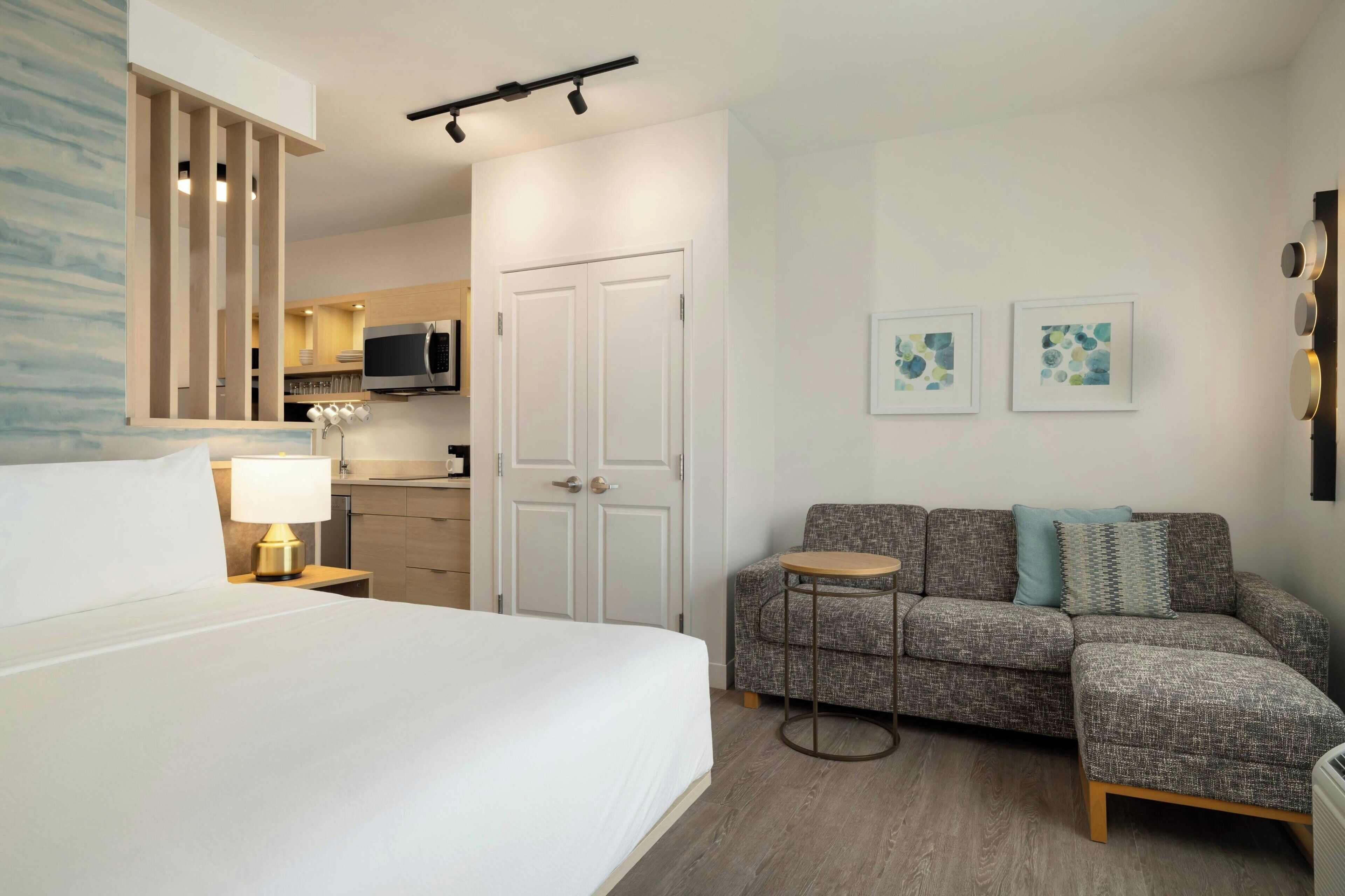 A hotel room with a bed, a sofa, a small table, a microwave, a cabinet, and a door.