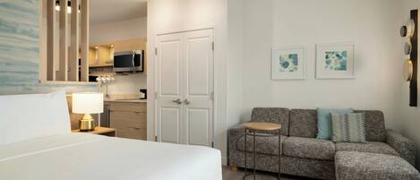 A hotel room with a bed, a sofa, a small table, a microwave, a cabinet, and a door.