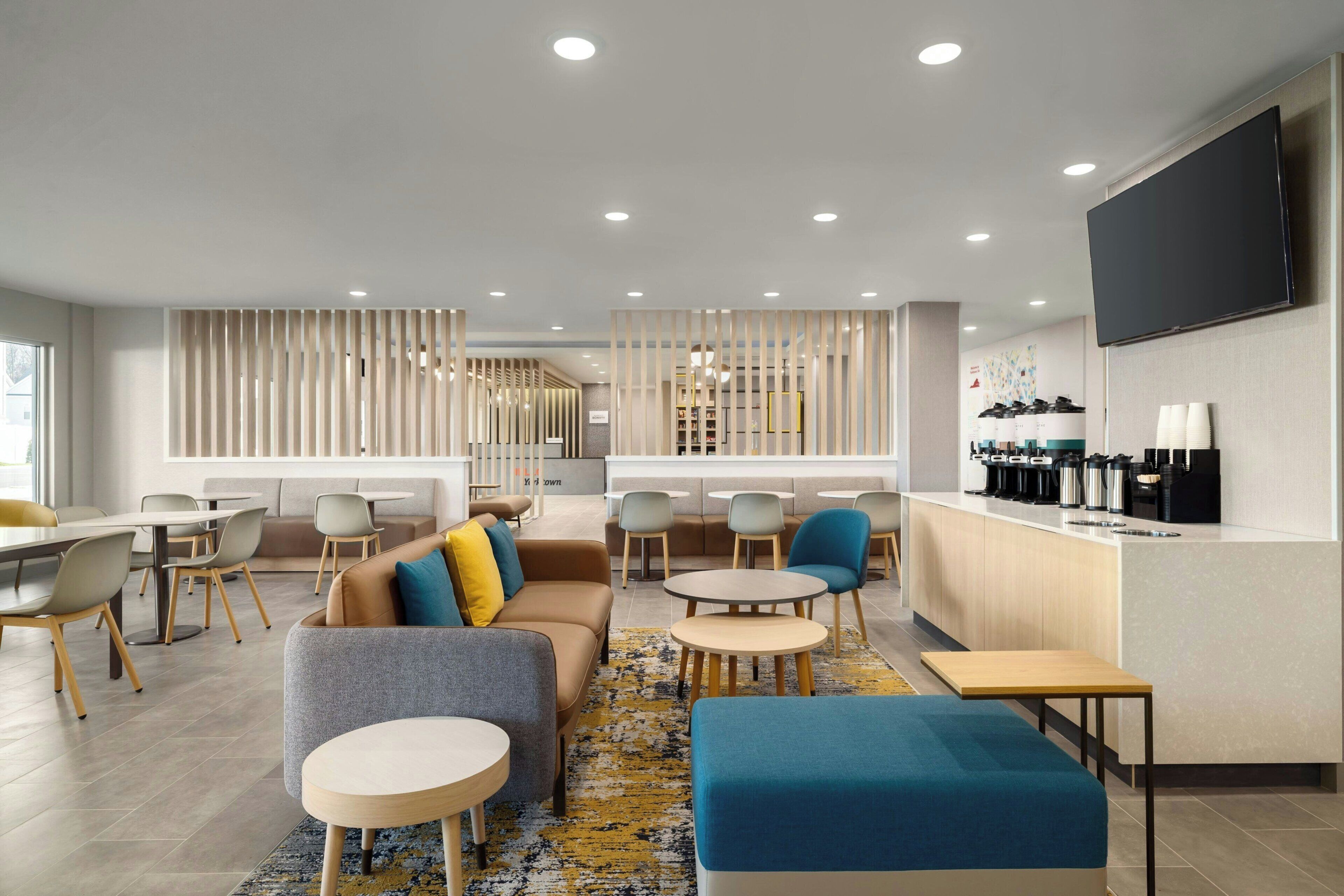 A modern hotel lobby with seating areas, a reception desk, and a coffee station.