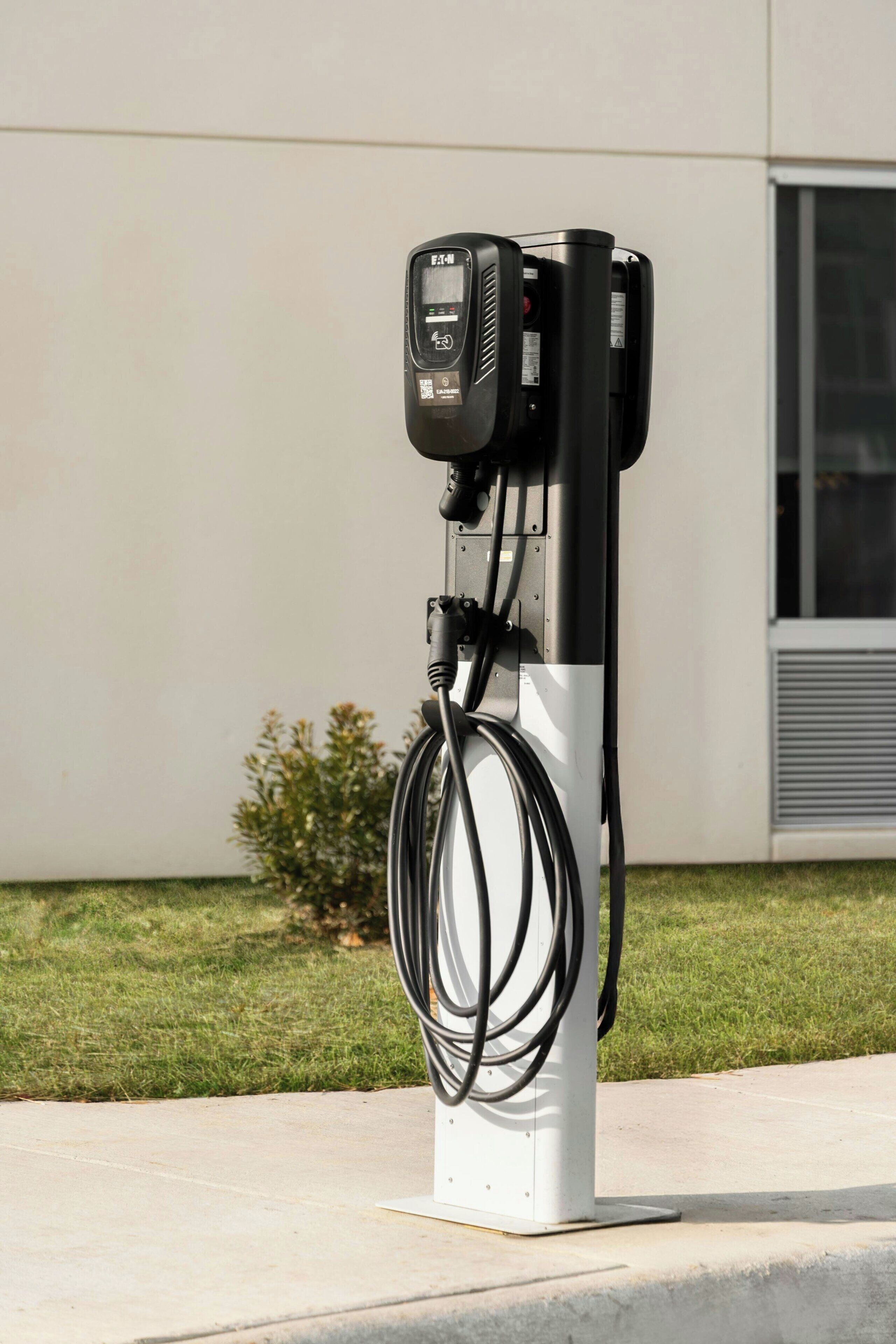 An electric vehicle charging station with a white base, a black charging unit, and a cable connected to it.