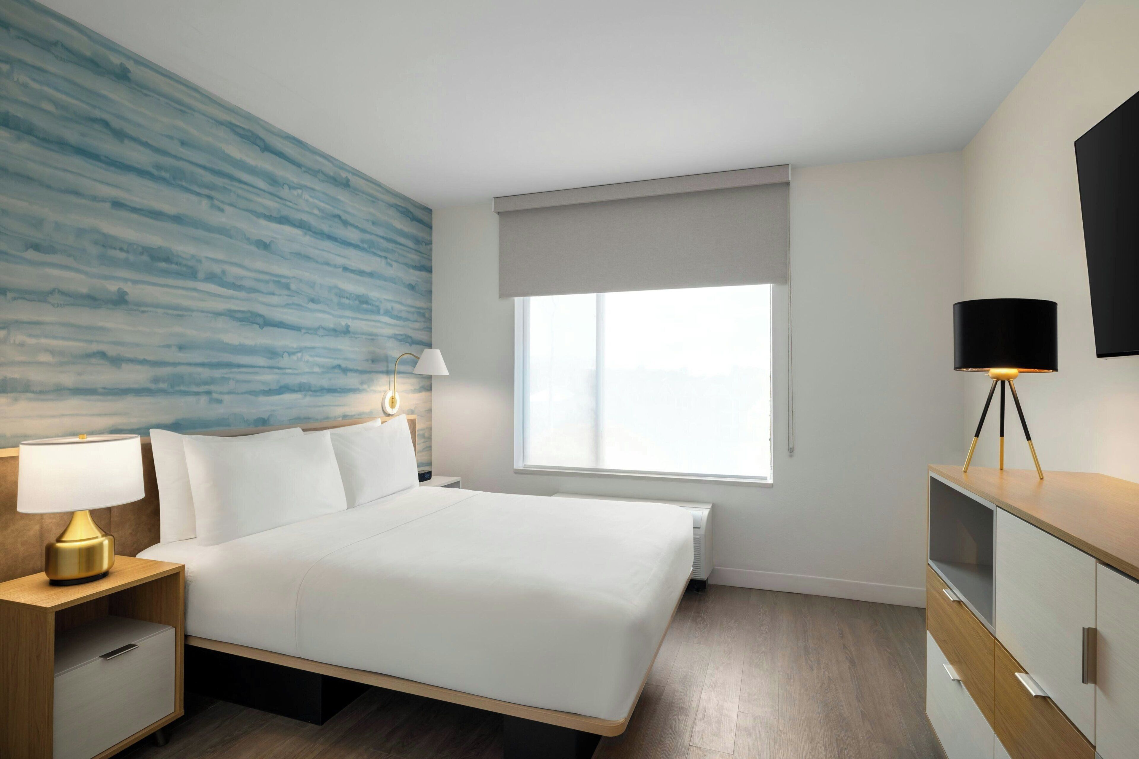 A hotel room with a bed, bedside tables, a lamp, a window, and a TV on a stand.
