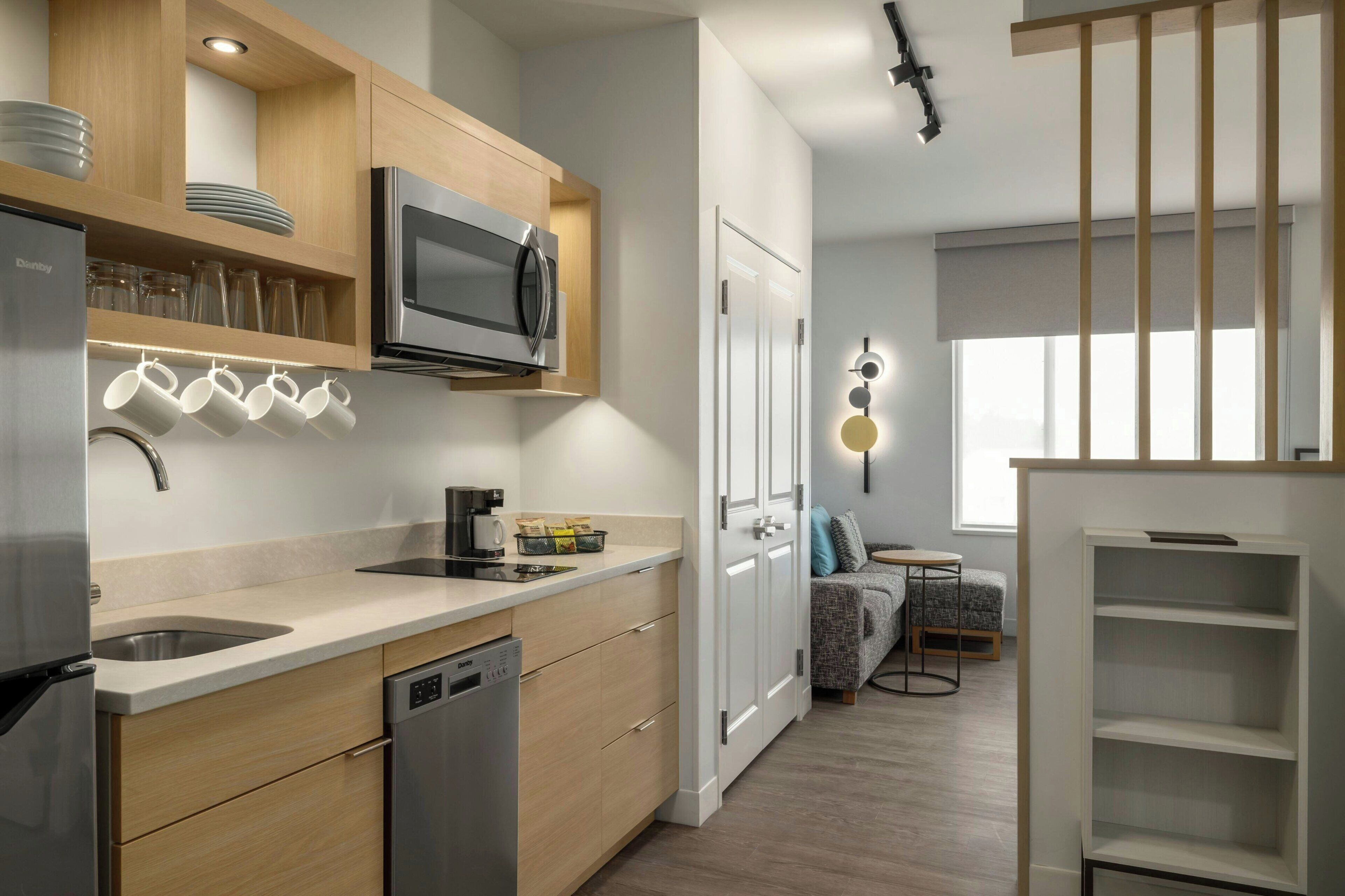 A modern kitchen with a dishwasher, microwave, and coffee maker. There is a dining area with a sofa and a table.