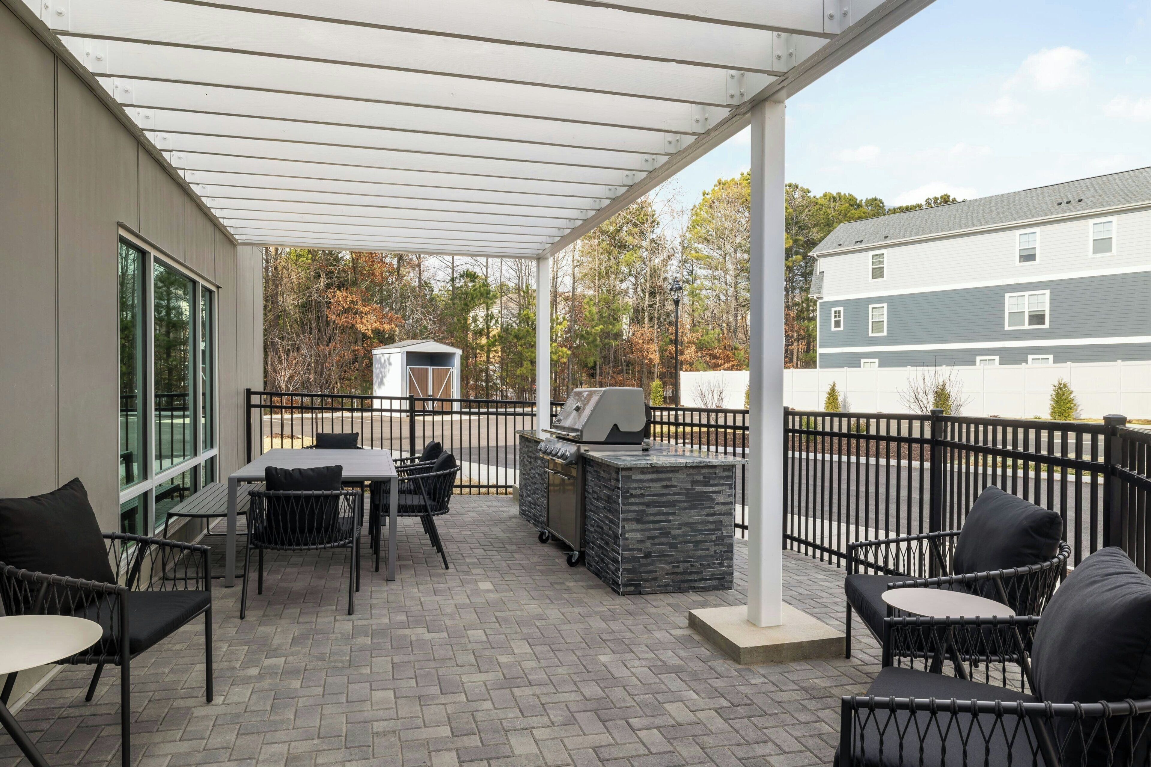 A covered patio area with outdoor furniture, a grill, and a small shed.