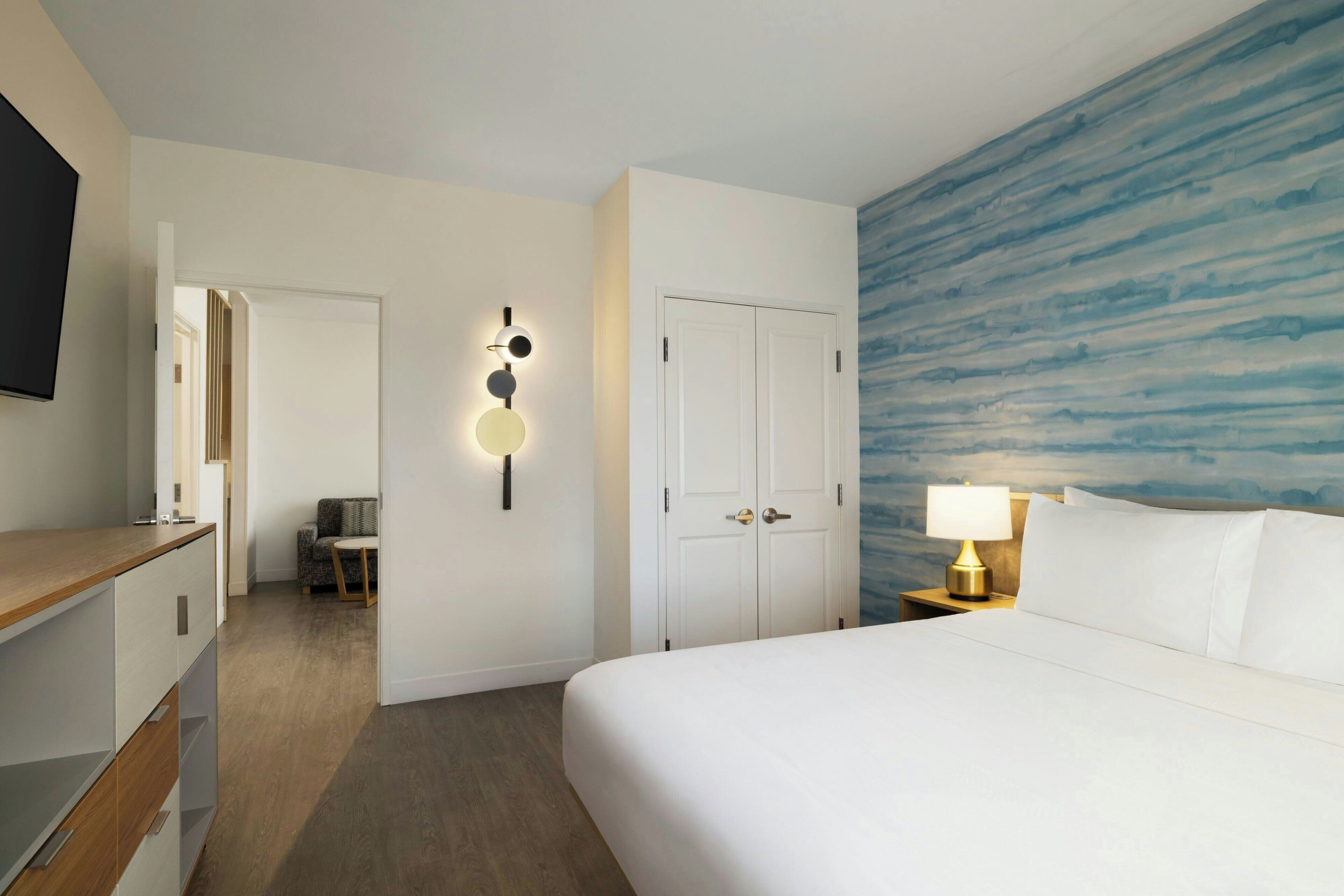 A hotel room with a bed, a desk, a chair, a wardrobe, and a wall-mounted TV.