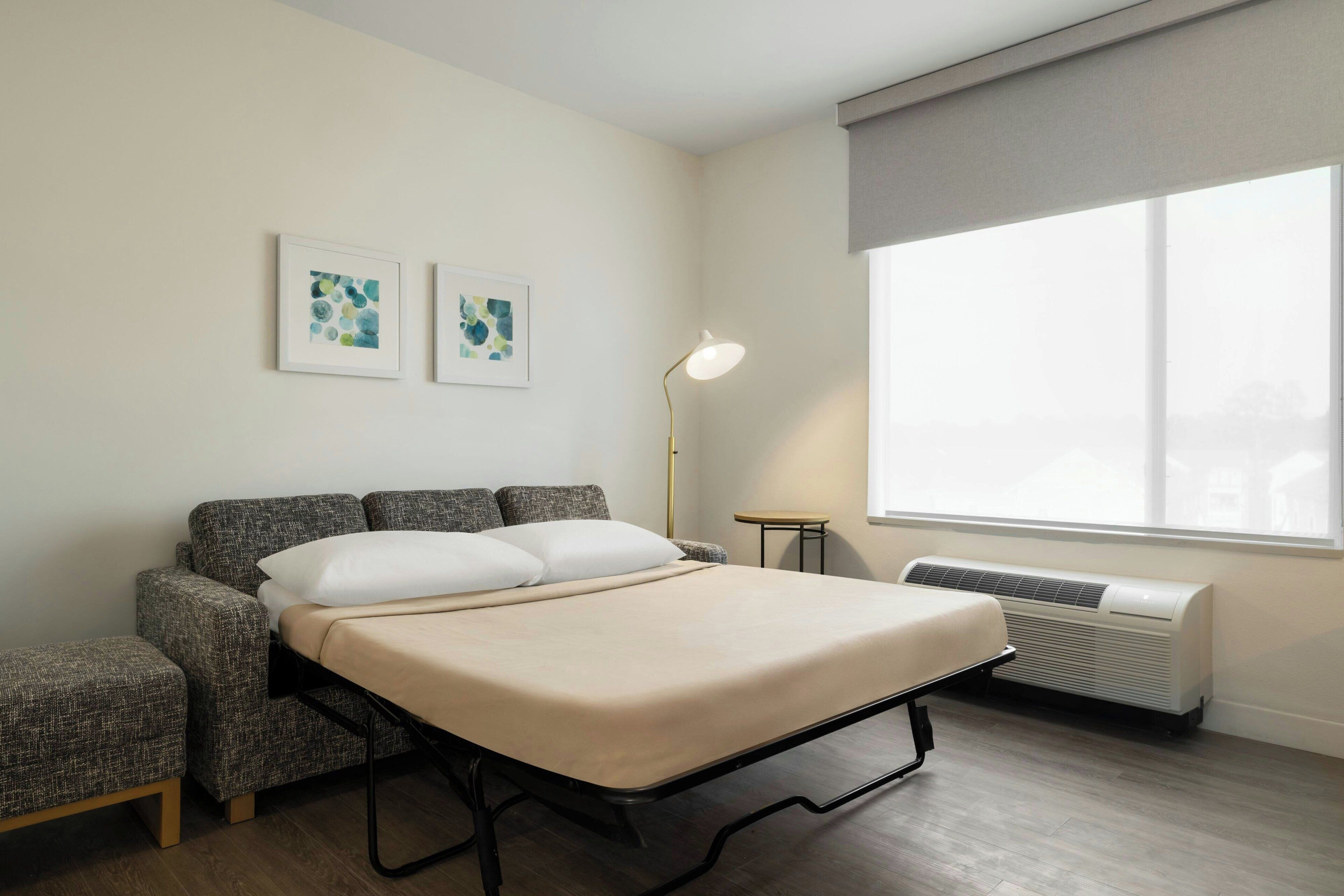 Un dormitorio con una cama, dos sillones, una lámpara de pie y una ventana con vistas.