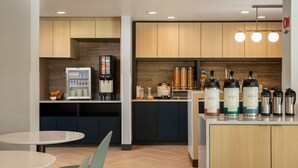 Een moderne keuken met houten kastjes, een koffieapparaat en een koffiehoek met dispensers met merklogo.