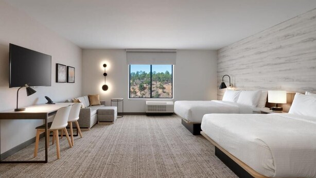 Een hotelkamer met een groot bed, een bureau met stoel, een televisie en een raam met uitzicht op bomen.