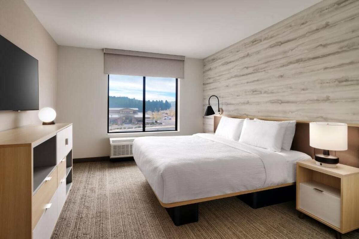 A modern hotel room with a large bed, a flat-screen TV, a desk, and a window with a city view.