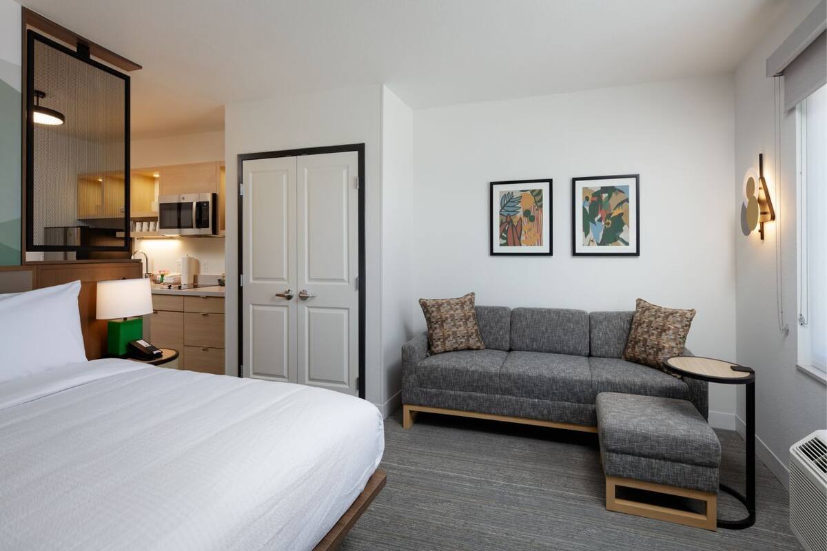 A hotel room with a bed, a gray sofa, a small table, and a microwave in the background.