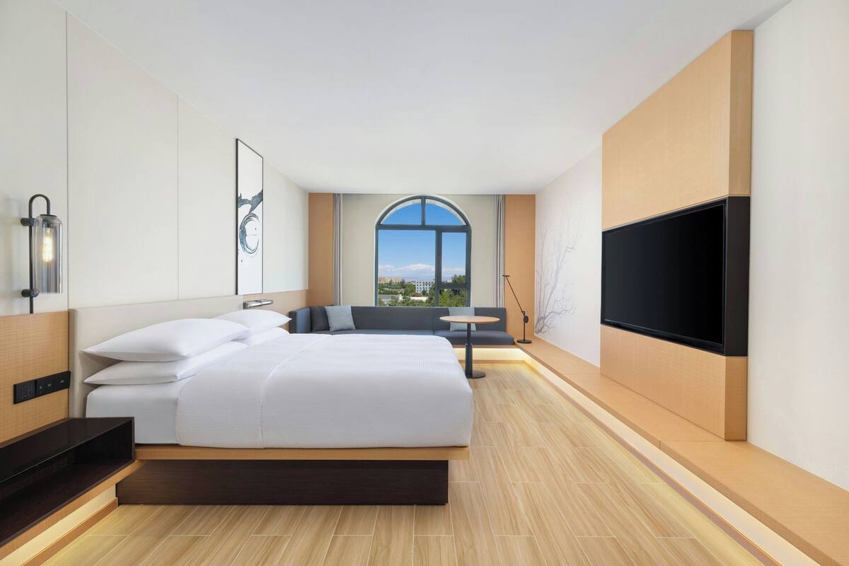 Ein modernes Hotelzimmer mit einem großen Bett, einem Flachbildfernseher, einer Sitzecke und einem Esstisch.