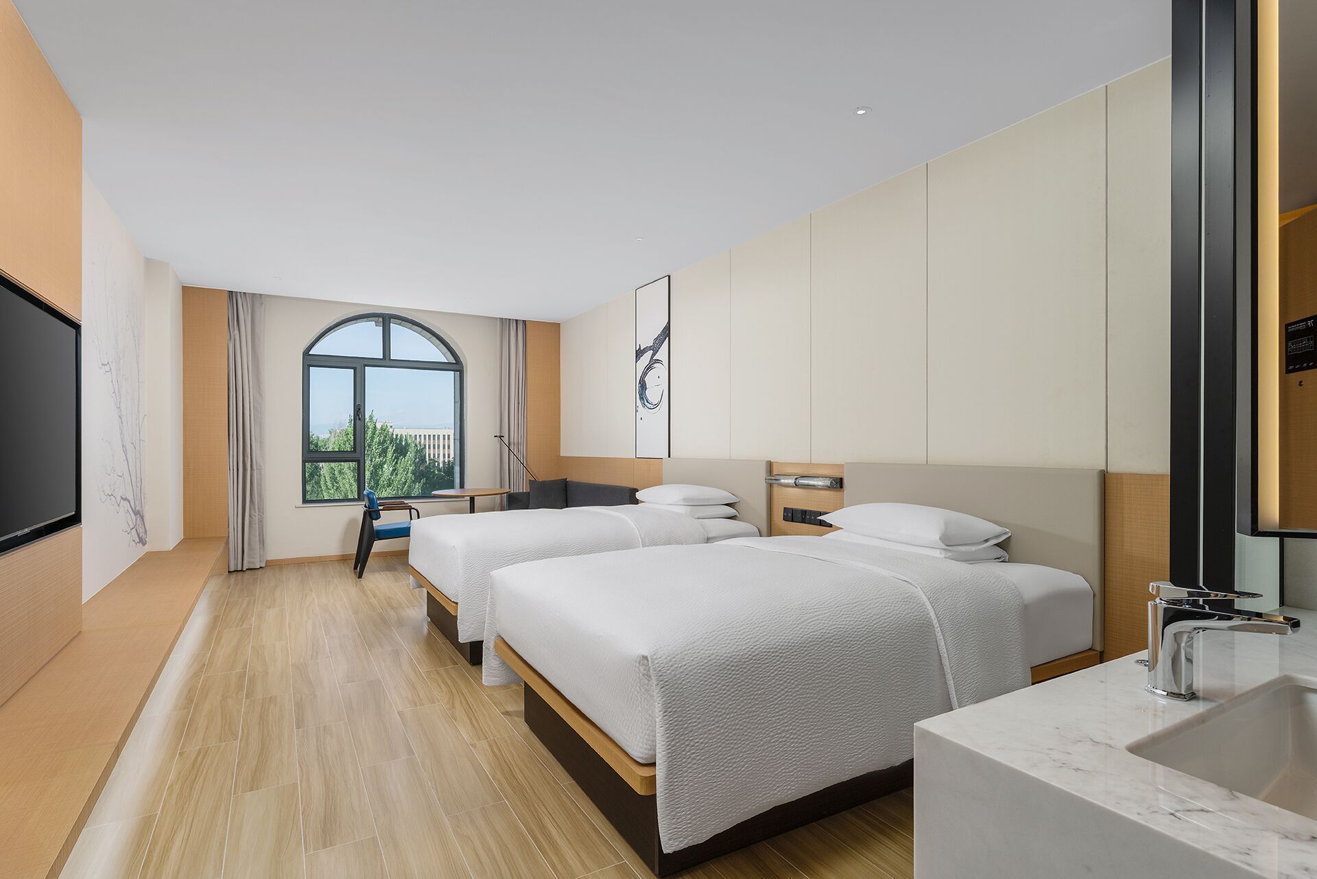 A hotel room with two beds, a large window, a desk, and a bathroom.