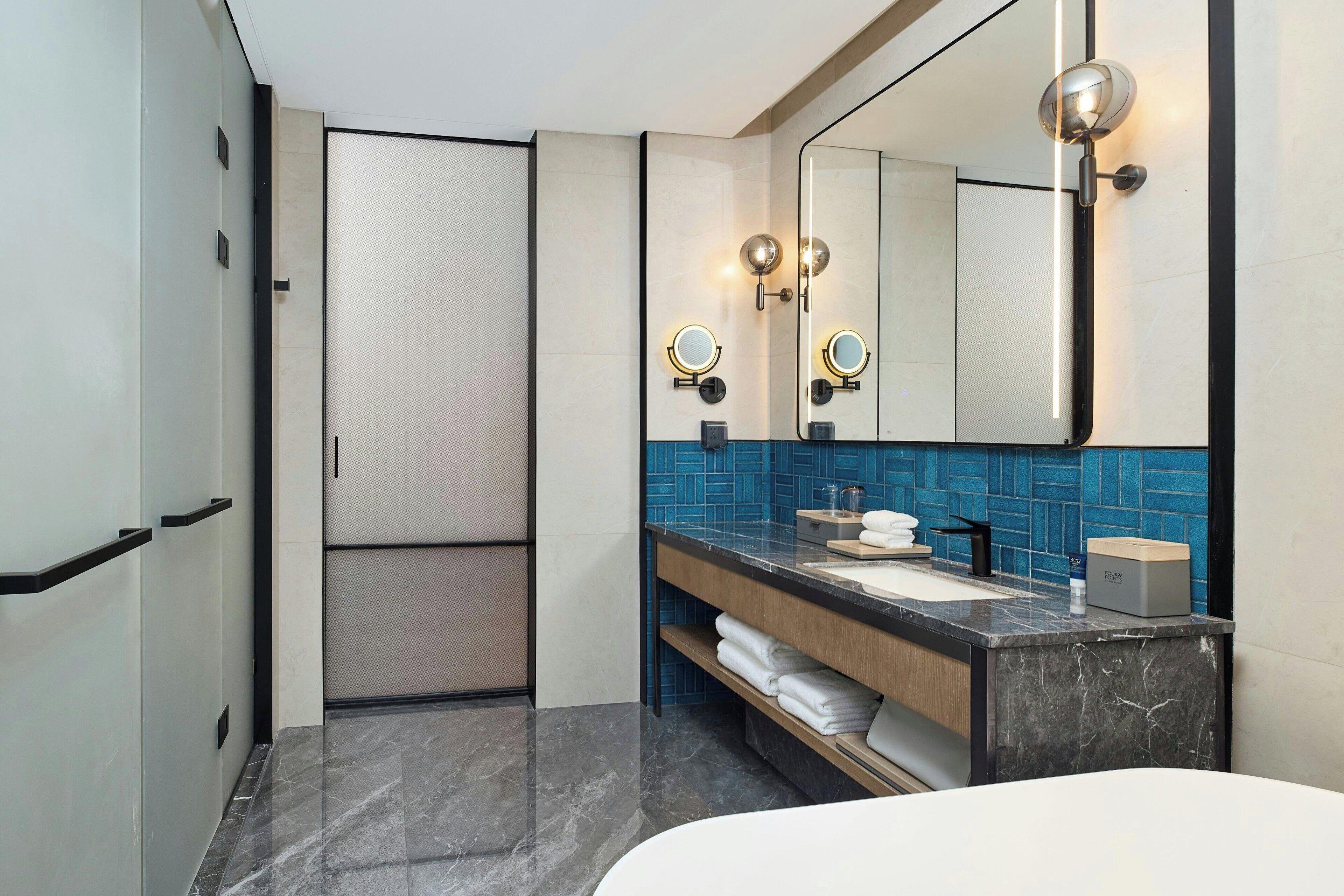 A modern bathroom with a large mirror, two round lights, a sink, and a towel rack.