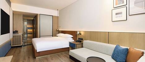 Una habitación de hotel moderna con una cama, un sofá, una mesita y un televisor montado en la pared.