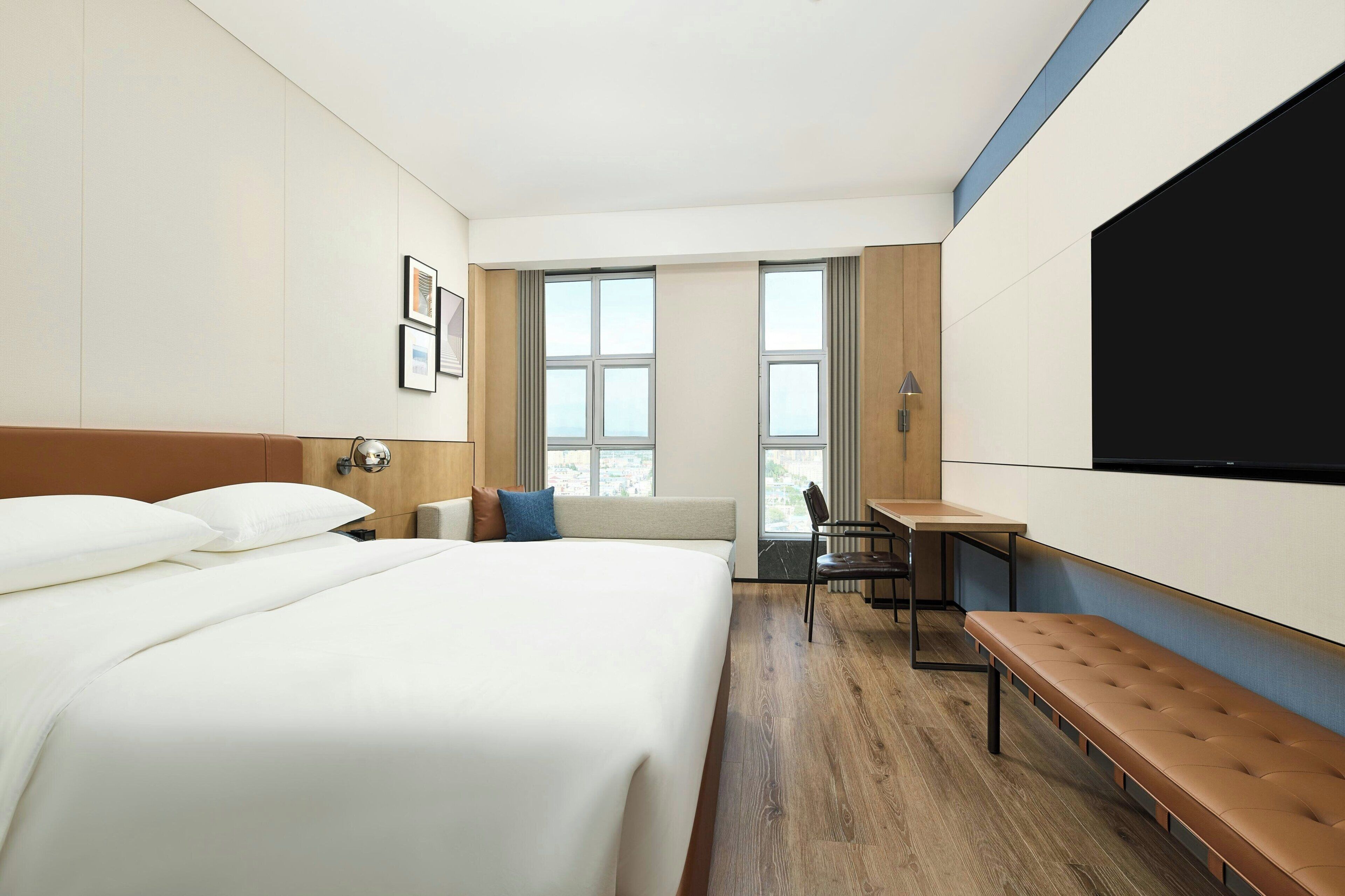 Una habitación de hotel con una cama grande, un escritorio, una banca y un televisor montado en la pared.
