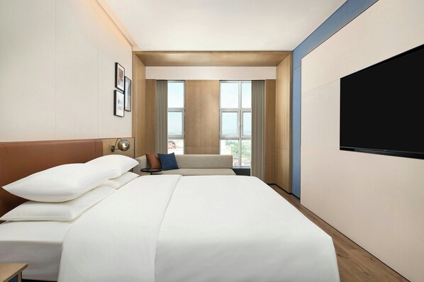 Een hotelkamer met een groot bed, een flatscreen televisie en uitzicht op de stad door grote ramen.