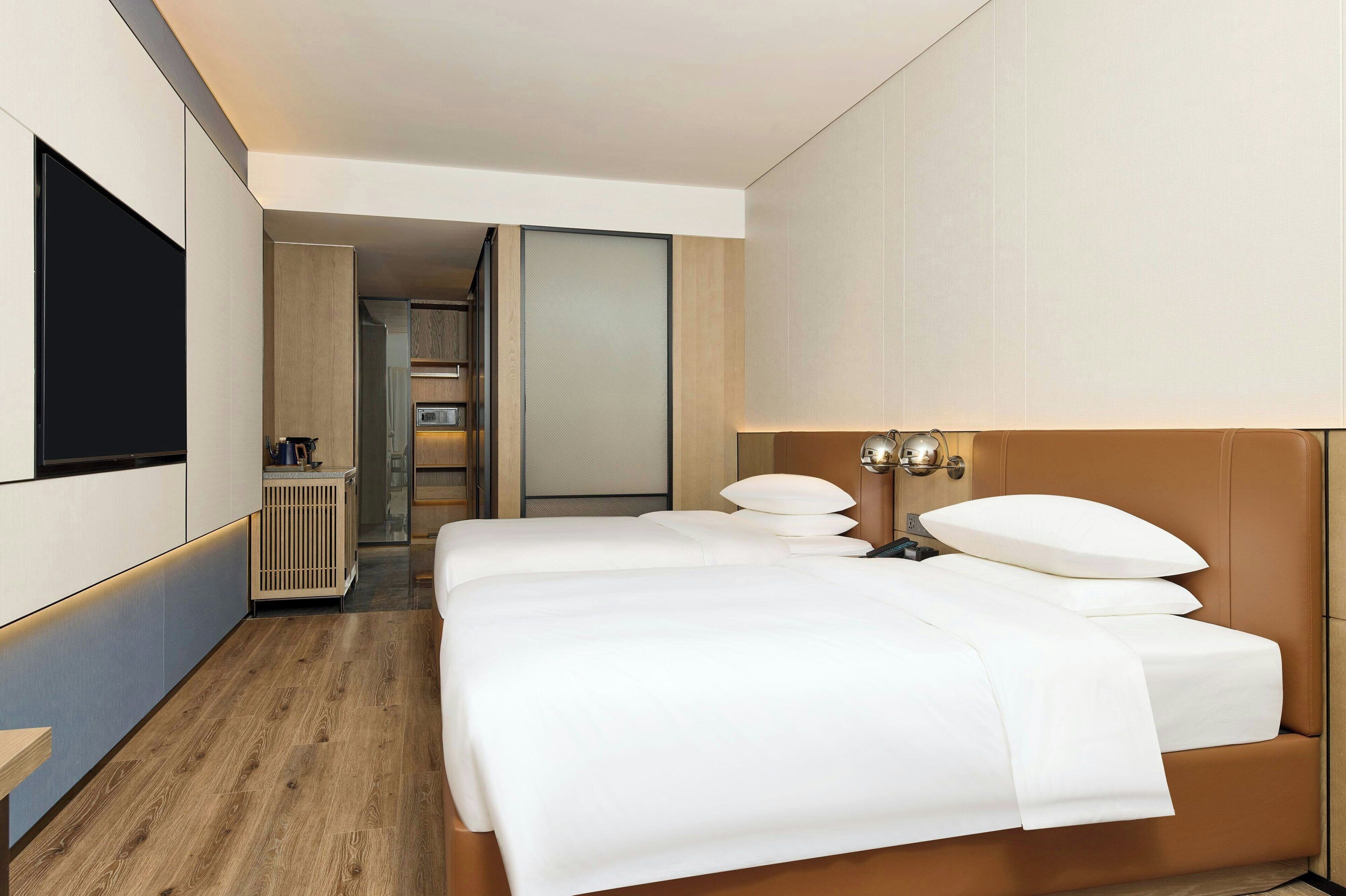A modern hotel room with a large bed, a flat-screen TV, and a view into the bathroom.