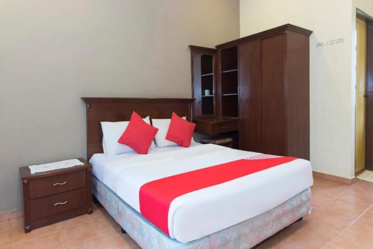 A neatly made bed with a red and white bedspread, a wooden nightstand with drawers, and a large wooden wardrobe.