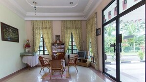A room with a tiled floor, a television, a table with chairs, and a window with curtains. - INB Resort Ayer Keroh Melaka (Malacca City)