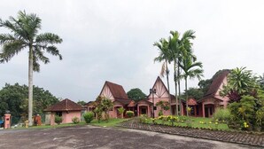 A row of pink-roofed buildings with a paved area in front, surrounded by palm trees and greenery. - INB Resort Ayer Keroh Melaka (Malacca City)