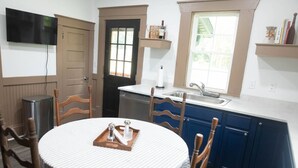 A compact kitchen with a dining area, featuring a round table with a tray, wooden chairs, a built-in oven, and a window with a view.