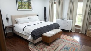 A bedroom with a bed, bedside table, bench, dresser, and a rug.