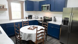 A kitchen with blue cabinets, a stainless steel refrigerator, a microwave, a stove, and a dining table with chairs.