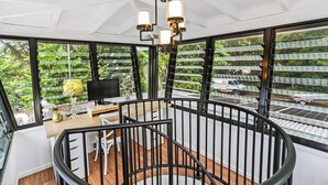 Un intérieur moderne avec un escalier en colimaçon, de grandes fenêtres donnant sur un paysage verdoyant et une route, ainsi qu'un bureau avec un téléviseur.