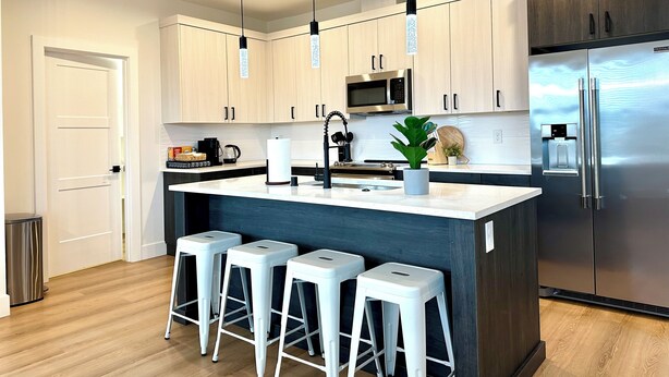 A modern kitchen with white bar stools, a stainless steel refrigerator, and a central island.