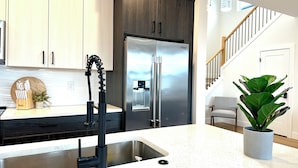 A modern kitchen with a stainless steel refrigerator, a sink with a black faucet, and a potted plant on the counter.