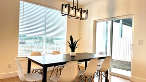 A modern dining area with a dark wooden table, white chairs, and a hanging light fixture.