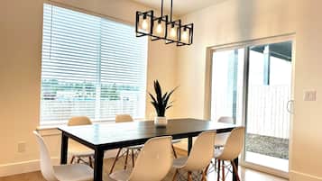 A modern dining area with a dark wooden table, white chairs, and a hanging light fixture.
