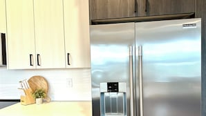 A stainless steel refrigerator with a water dispenser, wooden cabinets, and a countertop with a knife block and a small plant.
