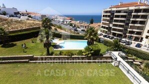 A residential area with a swimming pool, a view of the sea, and a multi-story building with balconies. - Infinity Waves by ACasadasCasas (Ericeira)