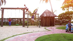 Un parque infantil con columpios, una red para escalar y una casita.