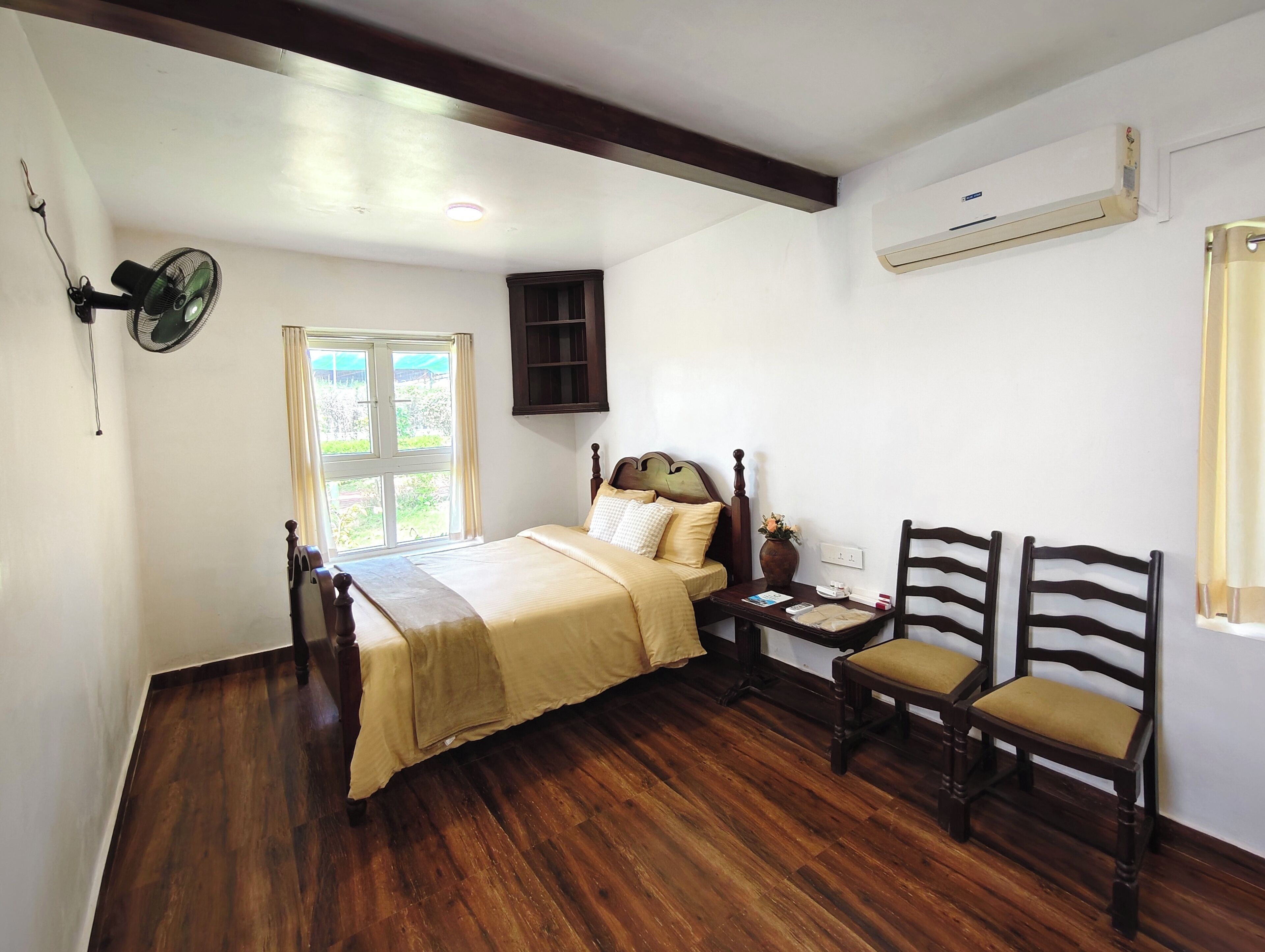 A bedroom with a wooden bed, a bedside table, a nightstand, two wooden chairs, a window, and an air conditioning unit.