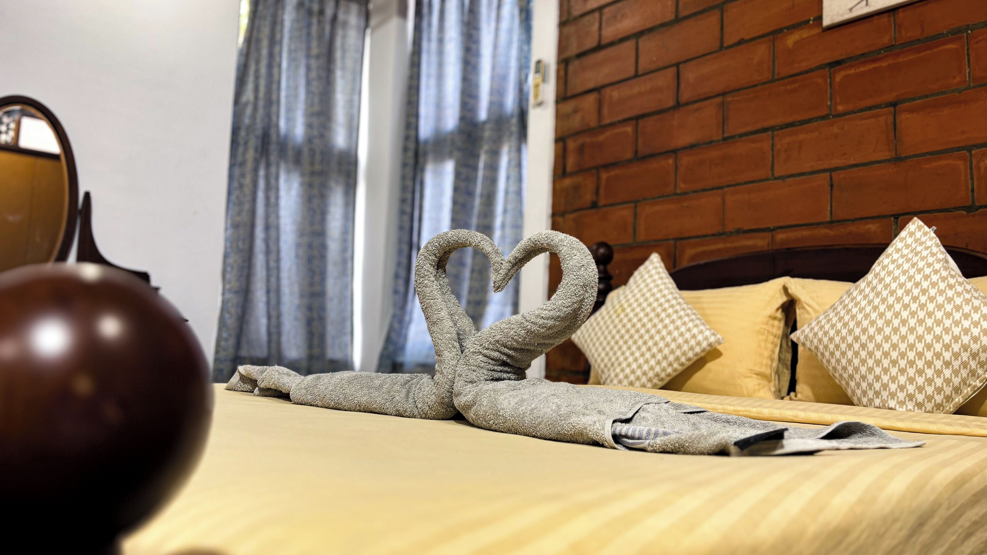 A bed with a towel arranged in a heart shape, a wooden headboard, and patterned pillows.