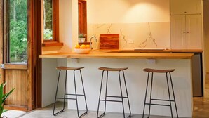 Une cuisine moderne dotée d’un grand îlot central, de trois tabourets, d’une fenêtre donnant sur un espace verdoyant et d’un meuble de rangement.