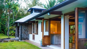 Une maison moderne avec une façade en pierre, des portes en bois et un espace cuisine visible à travers les portes ouvertes.