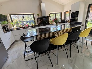 A modern kitchen with a central island, bar stools, and a view of the outdoors. - Large 4-bedroom villa, covered swimming pool, pétanque, volleyball... (Sainte-Anastasie-sur-Issole)