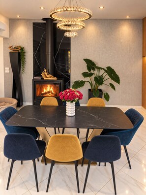 A modern dining area with a marble table, velvet chairs, a chandelier, a fireplace, and potted plants. - Villa Les Chênes Verts – Private Pool – Hot Tub – Provence – Sleeps 10 (Sainte-Anastasie-sur-Issole)