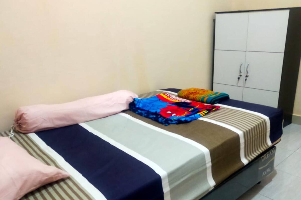 A neatly made bed with striped bedding, a colorful blanket, and a pink pillow.