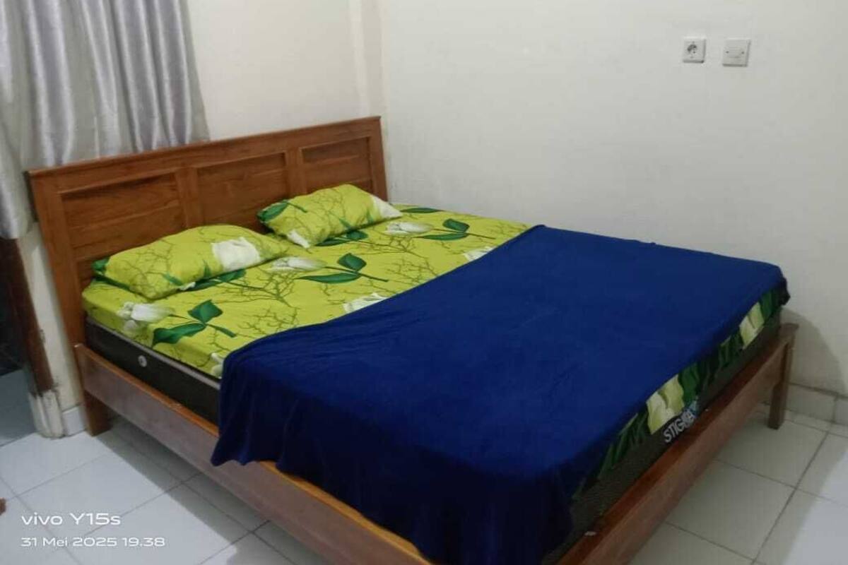 A single bed with a wooden headboard, a green and white patterned bedspread, and a blue blanket.