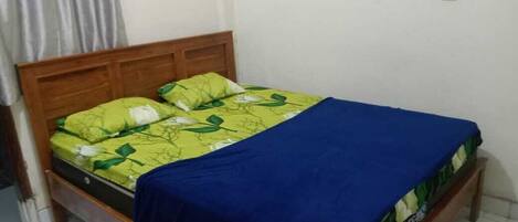 A single bed with a wooden headboard, a green and white patterned bedspread, and a blue blanket.
